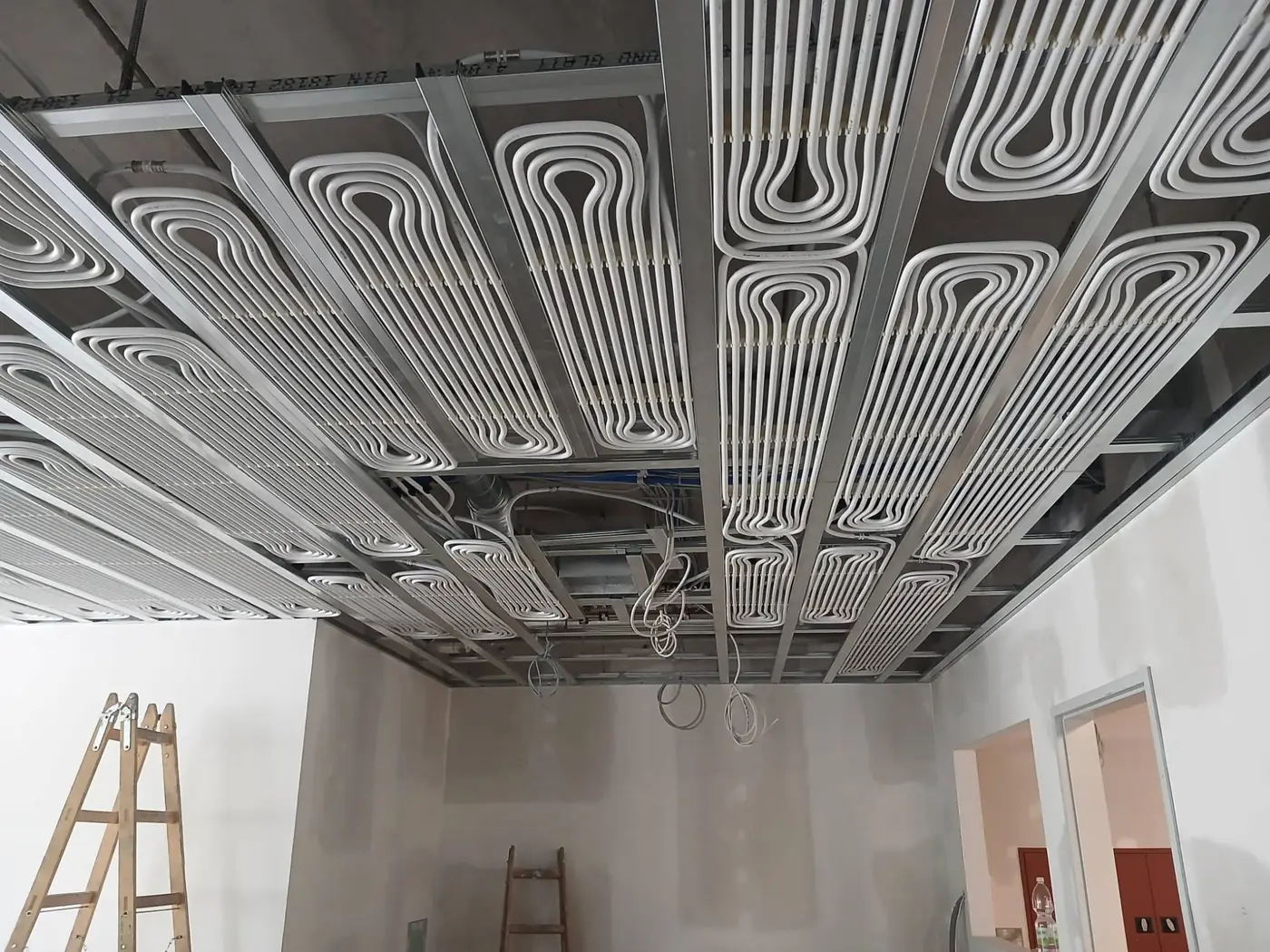 Deckenregister aus weißen Rohren zwischen Metallprofilen in einem Raum vor der Verkleidung