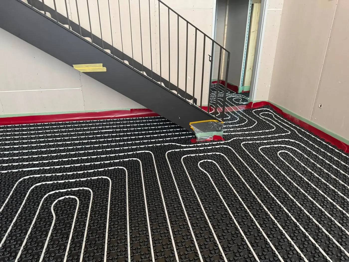 Heizrohre in Schlingen auf einer Noppenplatte im Rohbau neben einer Treppe